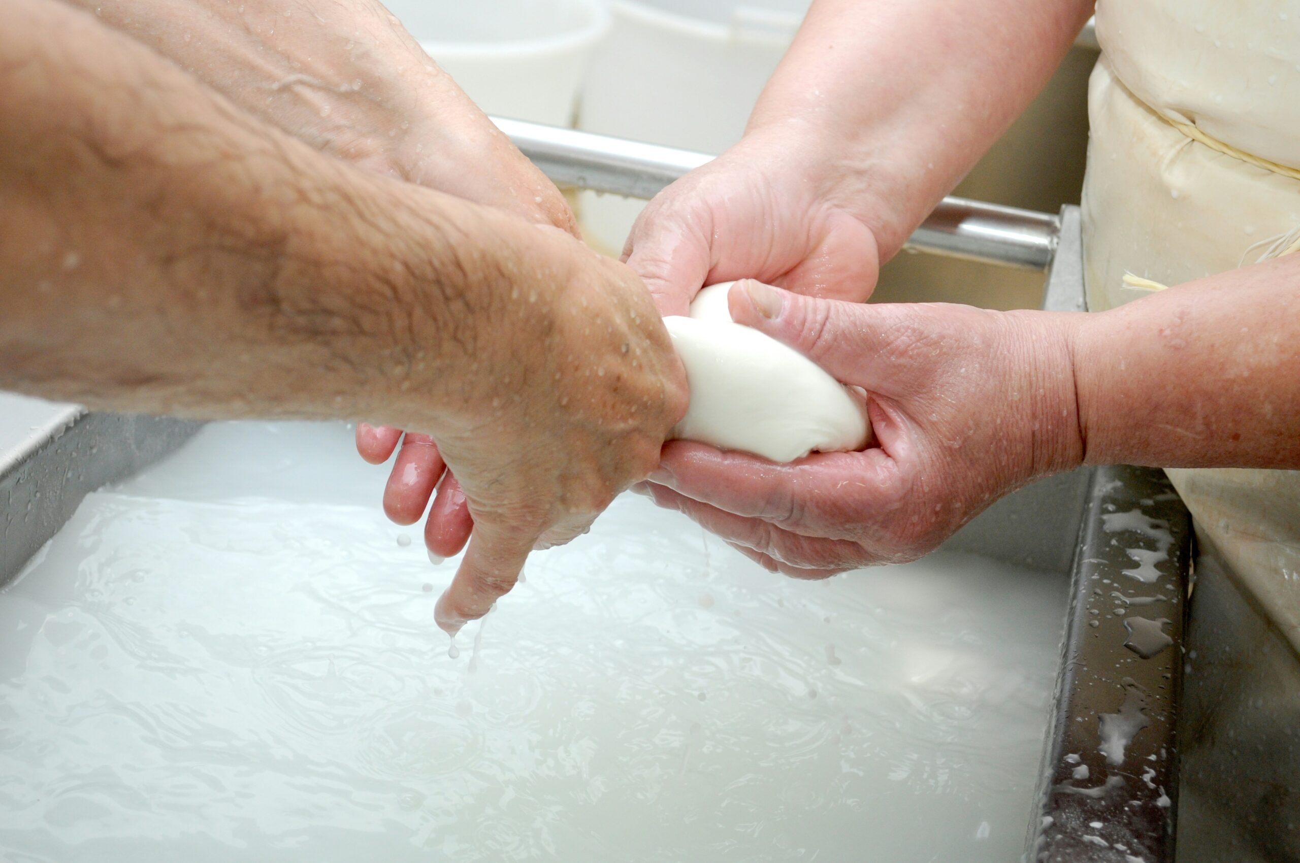 A person washing glass pet toys in warm soapy water at the sink.